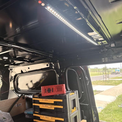 An Lumolux LED van light strip installed on the ceiling of a utility van, with storage tools and a workbench visible in the background.