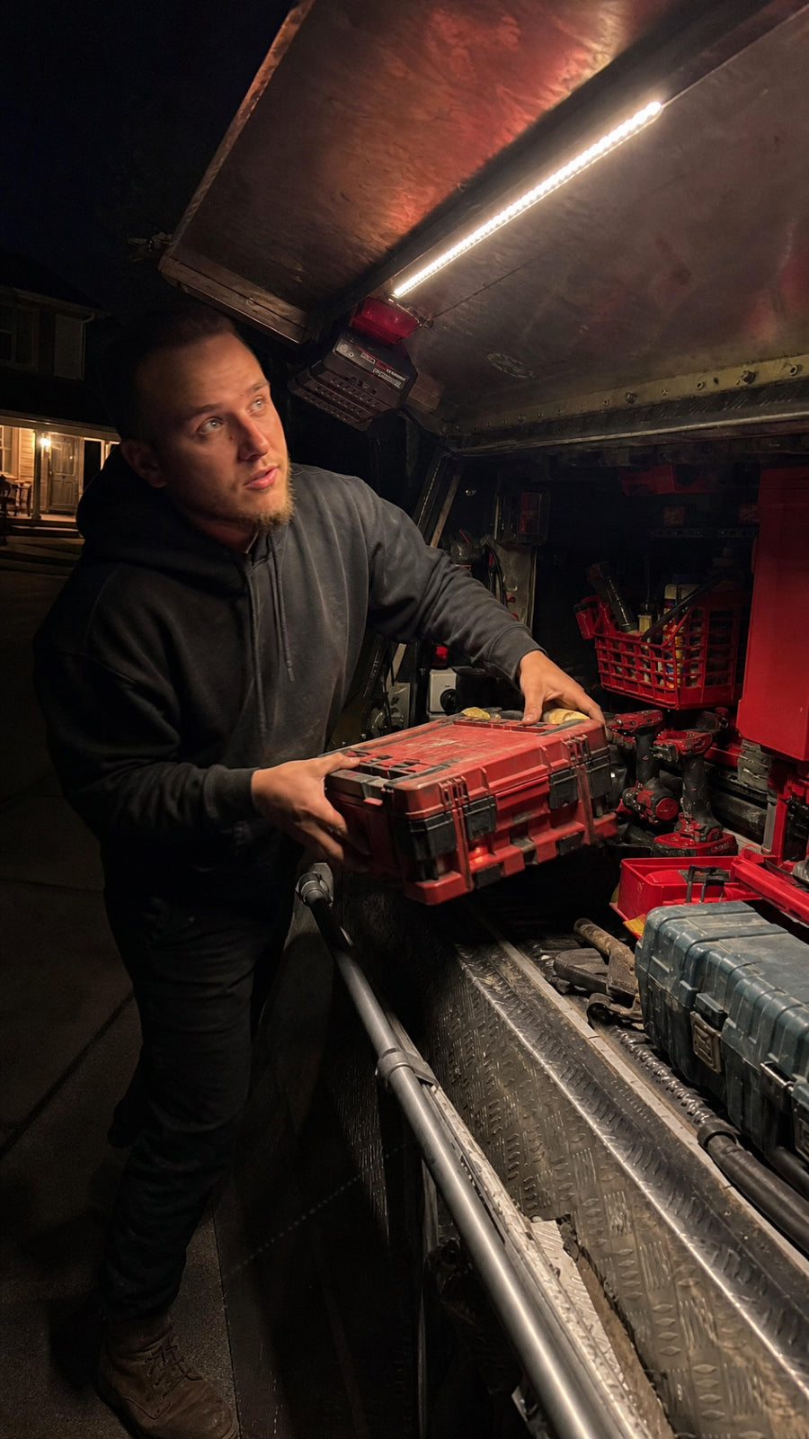 Contractor loading a tool box into a lit truck cap at night